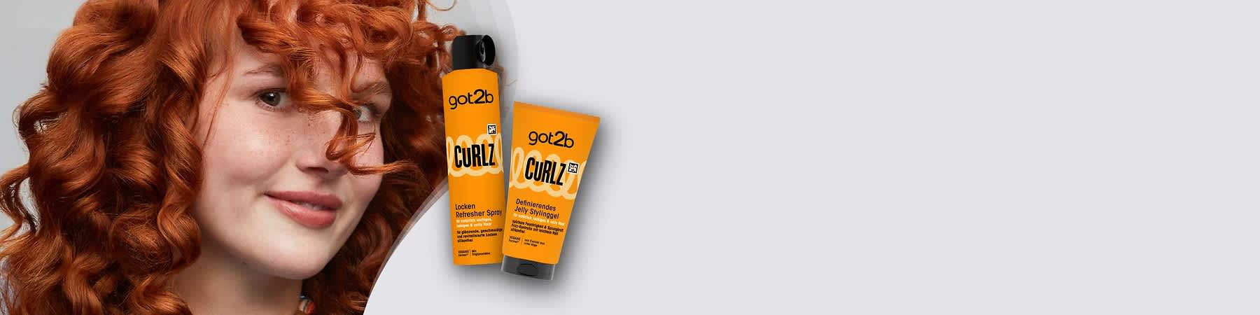 Zwei orangefarbene Haarpflegeprodukte der Marke got2b nebeneinander: links eine hohe Sprühflasche mit schwarzem Sprühkopf und der Aufschrift „got2b CURLZ Locken Refresher Spray“, rechts eine standfeste Tube mit schwarzem Verschluss und der Aufschrift „got2b CURLZ Definierendes Jelly Stylinggel“, im weißen Hintergrund das got2b-Logo oben rechts