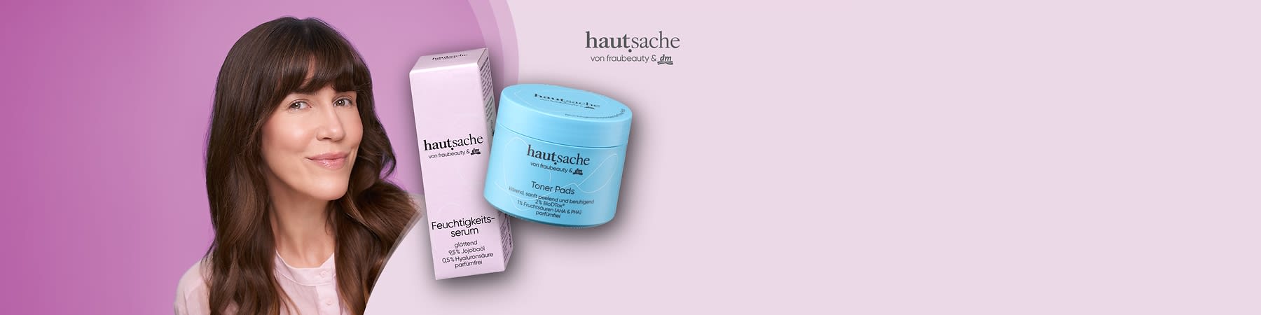 Brünette Frau mit lockeren, schulterlangen Haaren und rosa Bluse, im Vordergrund links ein hellblauer Tiegel mit der Aufschrift „hautsache von frau beauty & dm Toner Pads“ und rechts eine rosa Verpackung mit der Aufschrift „hautsache Feuchtigkeitsserum“ sowie dem kleinen Logo „hautsache von frau beauty & dm“