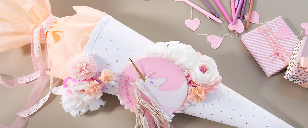 Kegelförmige Geschenkverpackung aus weißem Papier mit goldenen Punkten, verziert mit rosa und weißen künstlichen Blumen, einer rosa Quaste und einem runden Anhänger mit Einhornmotiv und dem Namen Samantha