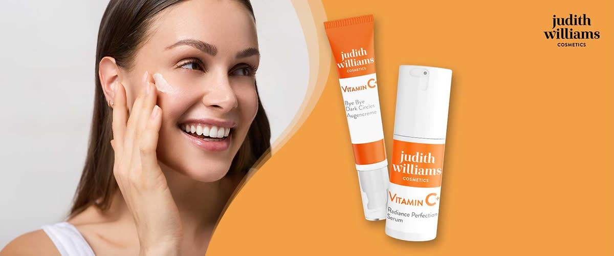 Zwei kosmetische Produkte von Judith Williams Cosmetics auf orangefarbenem Hintergrund: links ein schmales Tubenfläschchen mit orangefarbenem Deckel und dem Aufdruck „judith williams VITAMIN C Bye Bye Dark Circles Augencreme“, rechts eine weiße Airless-Pumpflasche mit orangefarbenem Etikett und der Aufschrift „judith williams VITAMIN C Radiance Perfection Serum“, oben rechts das Logo „judith williams COSMETICS“