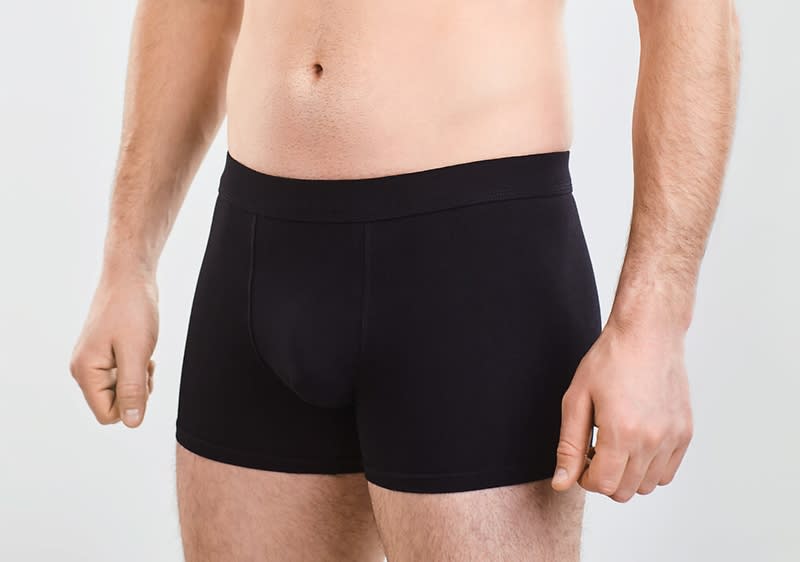Männlicher Torso und Oberschenkel in schwarzer Boxer-Shorts, Hände seitlich am Körper, neutraler heller Hintergrund