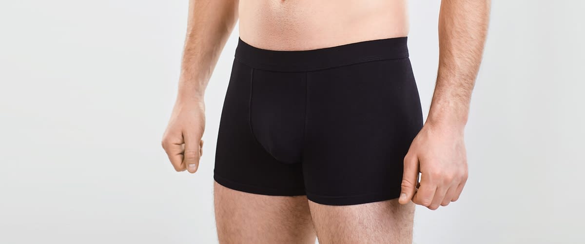 Männlicher Torso und Oberschenkel in schwarzer Boxer-Shorts, Hände seitlich am Körper, neutraler heller Hintergrund