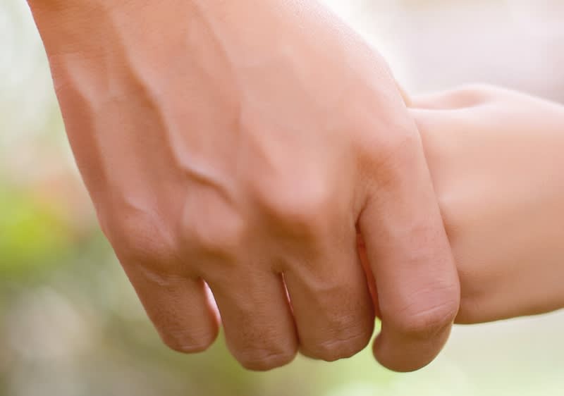 Erwachsener hält mit der Hand die Hand eines Kindes fest, Händchenhalten in Nahaufnahme