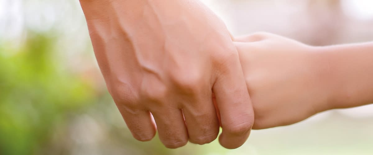 Erwachsener hält mit der Hand die Hand eines Kindes fest, Händchenhalten in Nahaufnahme