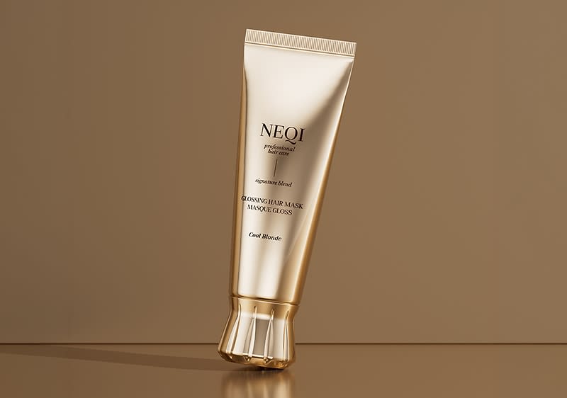 goldene Tube mit der Marke NEOI, Aufschrift „glossing hair mask“ und „Cool Blonde“, aufrecht stehend auf braunem Untergrund