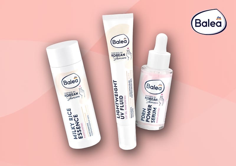 Drei Balea-Gesichtspflegeprodukte auf rosafarbenem Hintergrund: links eine weiße Flasche mit Aufschrift „Milky-Rice Essence“, in der Mitte eine Produktbox mit Logo und Schrift „PDRN Power Serum“, rechts eine Glasflasche mit Pipette und Etikett „PDRN Power Serum“