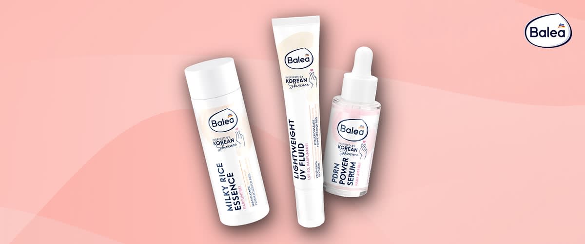 Drei Balea-Korean-Skincare-Produkte auf rosa Hintergrund: links weiße Flasche mit Aufschrift „Milk‑Rice Essence“, Mitte Karton mit Aufschrift „PDRN Power Serum“, rechts Glasfläschchen mit Pipette und Etikett „PDRN Power Serum“ und Balea-Logo