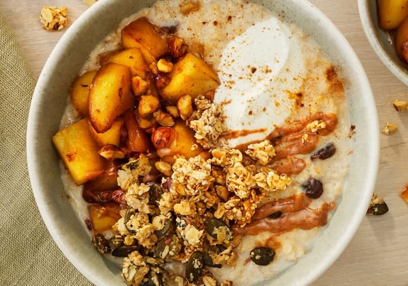 Schüssel mit Haferbrei, darauf Joghurt, karamellisierte Apfelstücke, knuspriges Müsli mit Nüssen und Kernen sowie Nussmusstreifen, leicht mit Zimt bestreut