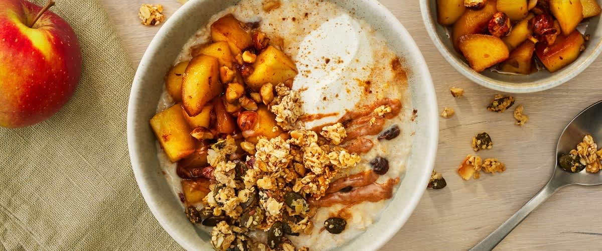 Schüssel mit Haferbrei, darauf Joghurt, karamellisierte Apfelstücke, knuspriges Müsli mit Nüssen und Kernen sowie Nussmusstreifen, leicht mit Zimt bestreut