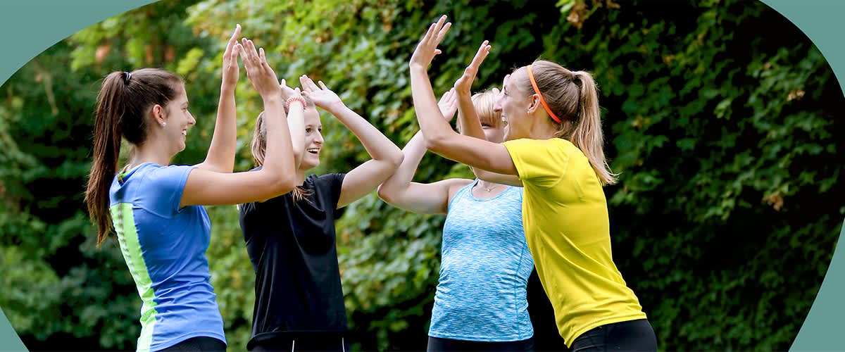 Vier junge Frauen in Sportkleidung stehen im Freien und geben sich gleichzeitig Highfives.