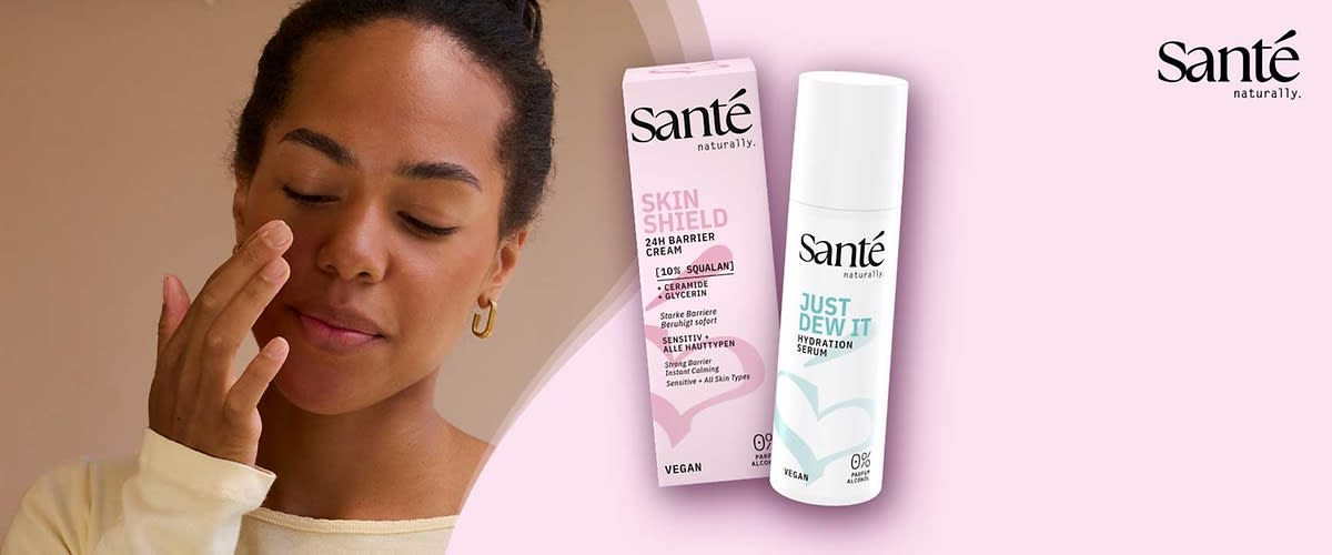 Zwei vegane Hautpflegeprodukte der Marke Santé auf rosa Hintergrund: links eine rosa Verpackung mit der Aufschrift „Skin Shield 24H Barrier Cream [10% Squalan]“ und rechts eine weiße Pumpflasche mit der Aufschrift „Just Dew It Hydration Serum“ sowie Markenlogo oben rechts