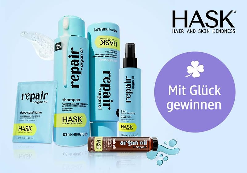 Mehrere hellblaue HASK Haarpflegeprodukte mit Aufschrift „repair + argan oil“: Shampooflasche, Spray, Tube, Sachet und kleine Ampulle, rechts oben schwarz das HASK-Logo, rechts ein lilaner Kreis mit weißer Blütengrafik und Text „Mit Glück gewinnen“