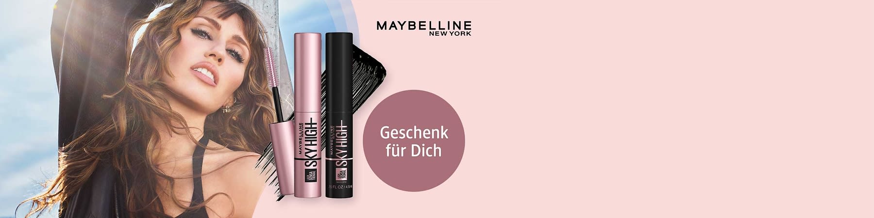 Zwei Maybelline Sky High Mascaras in metallic-rosé und schwarz vor hellrosa Hintergrund, links Mascara-Bürste mit Wimperntusche, rechts runder rosa Kreis mit weißem Text „Geschenk für Dich“ und Markenlogo „MAYBELLINE NEW YORK“ oben rechts