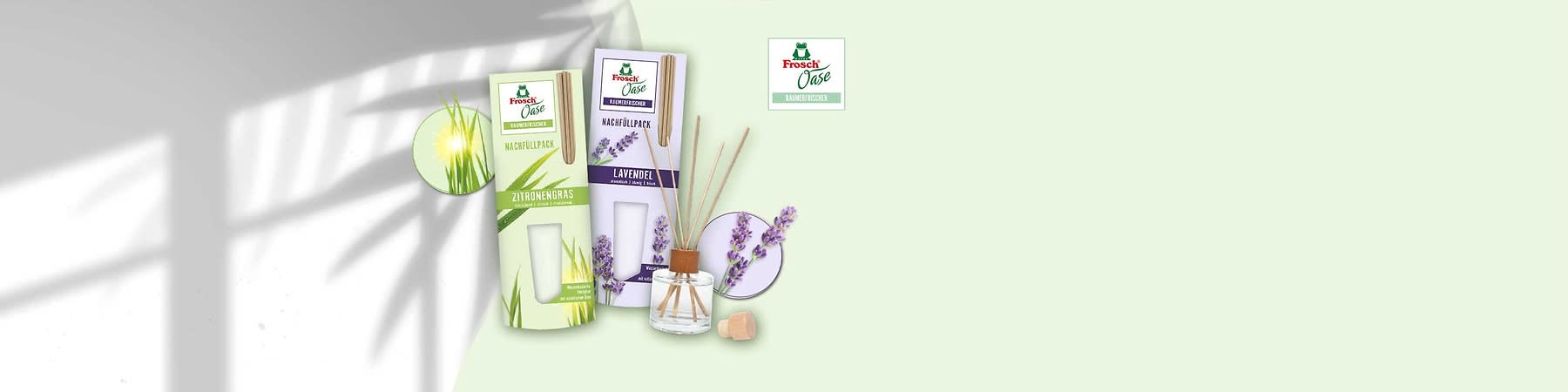 Zwei Frosch Oase Raumduft-Nachfüllpacks nebeneinander: links grünes Paket „Zitronengras“, rechts lilafarbenes Paket „Lavendel“, davor Glasflakon mit Holzstöckchen und Holzkorken, oben rechts kleines Frosch Oase-Logo