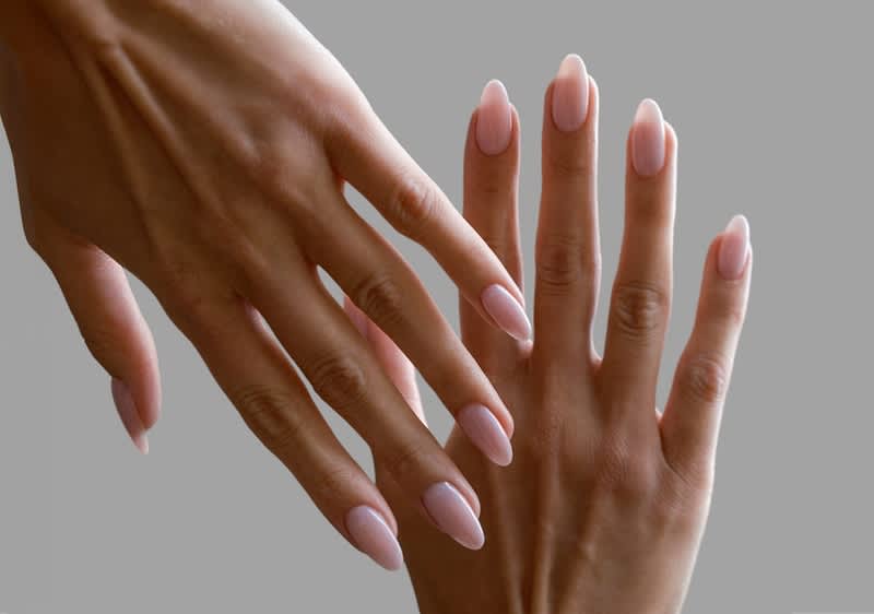 Zwei weiblich wirkende Hände mit hellrosa, mandelförmig gefeilten Gelnägeln, eine Hand leicht über der anderen gehalten