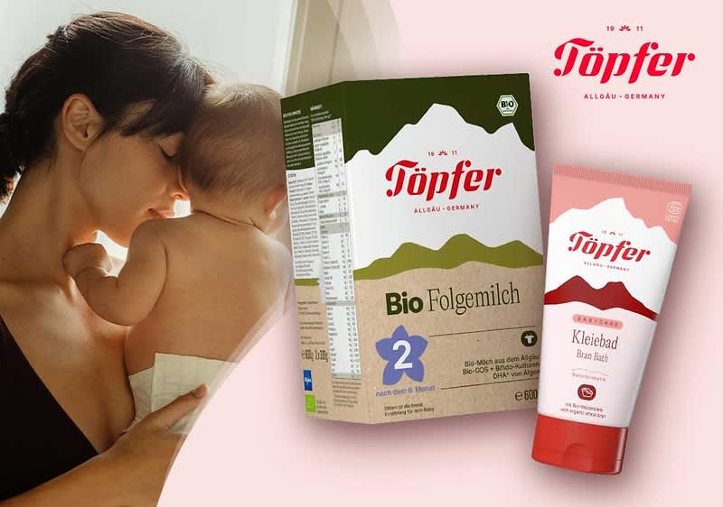 Mutter hält nacktes Baby auf der Schulter, daneben zwei Töpfer-Produkte: eine rosa Tube „Kleiebad Bran Bath“ und eine grüne Packung „Bio Folgemilch 2“ mit Töpfer-Logo oben rechts