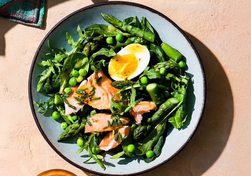 Salat mit grünem Spargel, Erbsen und Blattspinat, dazu Stücke von Lachs und ein halbiertes weichgekochtes Ei auf einem runden Teller