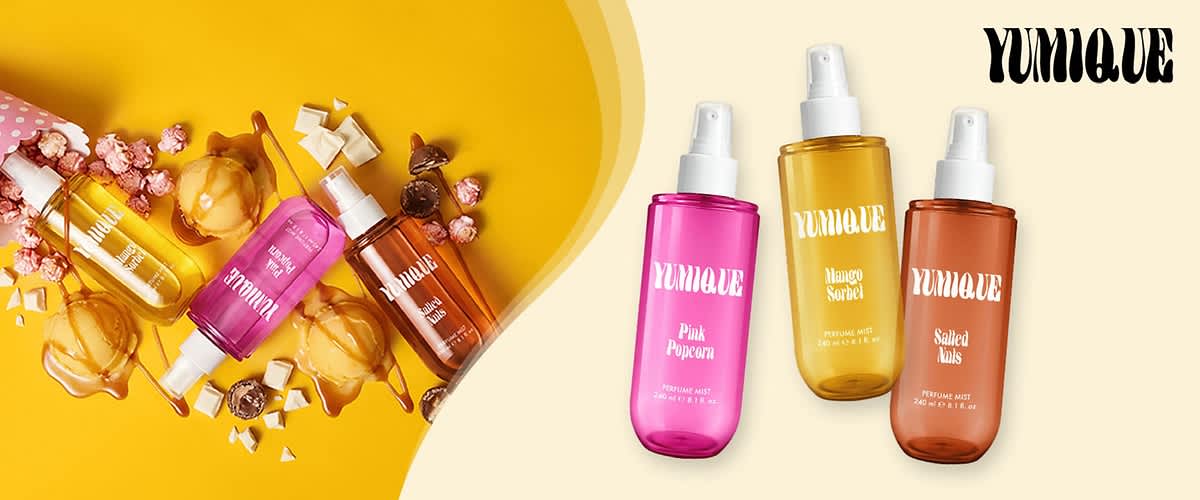Drei Duftsprays der Marke YUMIQUE in transparenten Kunststoffflaschen mit Sprühkopf: links pink beschriftet „Pink Popcorn“, mittig gelb beschriftet „Mango Sorbet“, rechts orange-braun beschriftet „Salted Nuts“; links daneben eine Anordnung von Kugeln, Karamell, Schokolade und weißer Schokolade auf gelbem Hintergrund