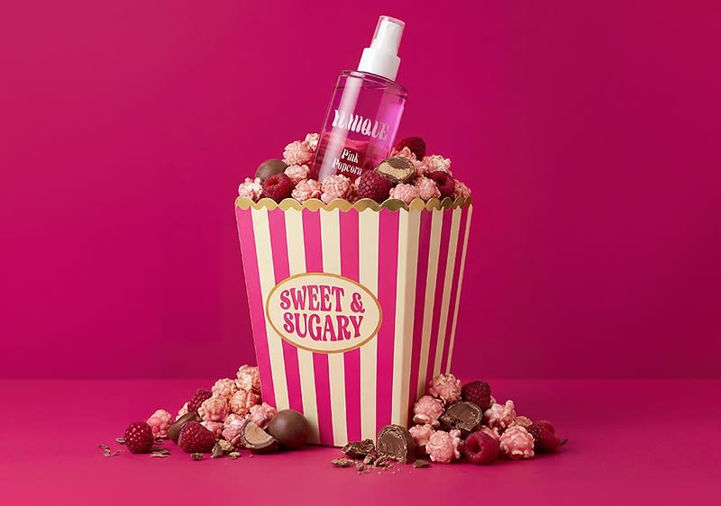 Popcorntüte mit rosa-weißen Streifen und Aufschrift „SWEET & SUGARY“, gefüllt mit pink-gefärbtem Popcorn, Schokoladenstücken und Himbeeren, oben ein rosa Sprayflakon mit Aufschrift „Pink Paradise“