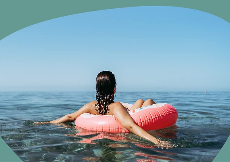 Frau sitzt in einem pinken Schwimmring auf dem ruhigen Meer, Blick aufs offene Wasser