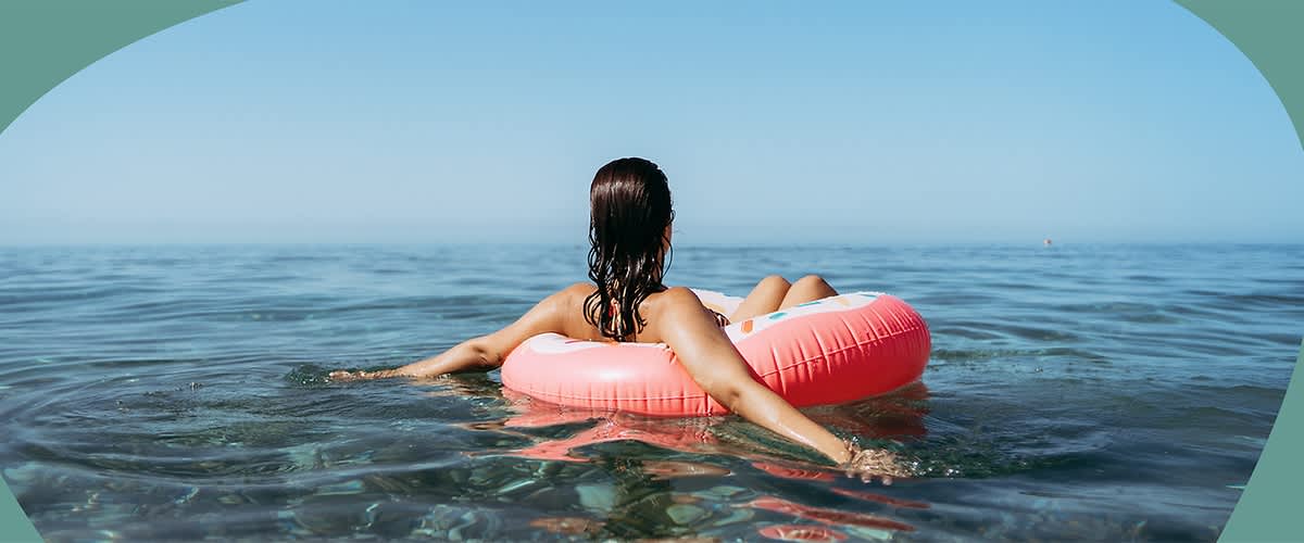 Frau sitzt in einem pinken Schwimmring auf dem ruhigen Meer, Blick aufs offene Wasser