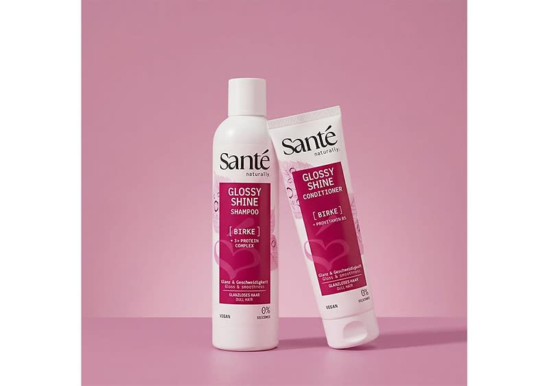 Zwei rosa-weiße Haarpflegeprodukte der Marke Santé: links eine weiße Flasche mit Aufschrift „Glossy Shine Shampoo“, rechts eine passende Tube mit Aufschrift „Glossy Shine Conditioner“, beide mit Herzmotiv und zusätzlicher Textzeile „Birke“ auf rosafarbenem Hintergrund