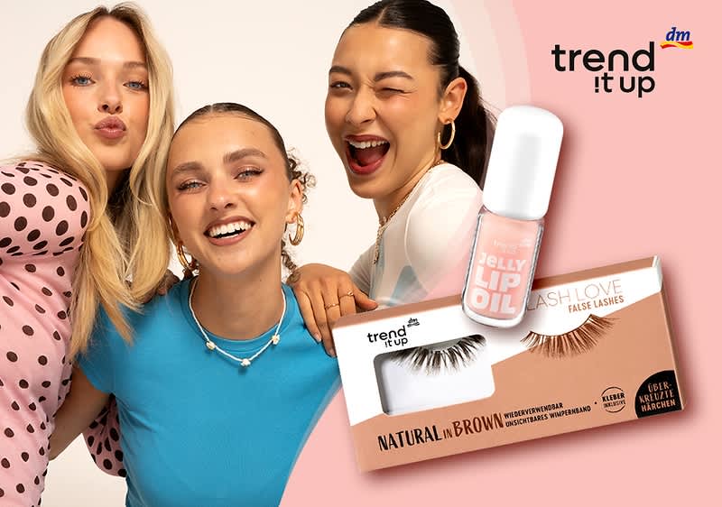 Drei junge Frauen posieren eng nebeneinander, rechts daneben Lippenstift-Glasflakon mit der Aufschrift „JELLY LIP GLOSS“ und darunter Verpackung falscher Wimpern „BIG LASH LOVE“ in der Farbbezeichnung „NATURAL in BROWN“, oben rechts Logo „trend it up“