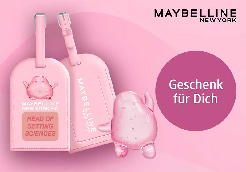 Rosafarbene Reisetaschen-Anhänger mit Maybelline New York-Branding, dazu eine kleine rosafarbene Comic-Figur und ein violetter Kreis mit dem weißen Text „Geschenk für Dich“
