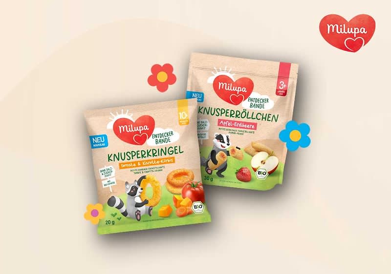 Zwei Milupa Produktverpackungen mit Knusperringen und Knusperböllchen. Links eine Packung mit der Aufschrift „Knusperkringel Banane & Karotte-Citrus“, rechts „Knusperböllchen Apfel-Erdbeere“. Beide Verpackungen zeigen bunte Illustrationen von Obst und Tieren. Oben rechts das Milupa-Logo.