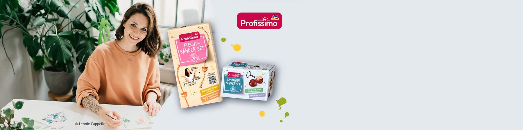 Frau sitzt lächelnd am Tisch und zeichnet Blumen, daneben zwei Profissimo Bastelsets in Verpackung: ein „Flechtbänder Set“ und ein „Kastanien Bohrer Set“ mit dm-Profissimo-Logo