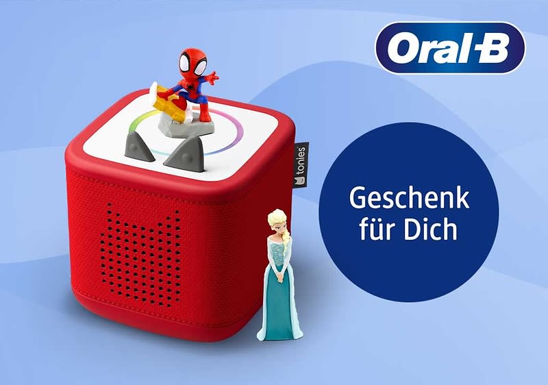 Rotes quadratisches Toniebox-ähnliches Lautsprechergerät mit schwarzen Bedienknöpfen oben, darauf eine Spider-Man-Figur, daneben eine Elsa-Figur, rechts ein blauer Kreis mit weißer Schrift „Geschenk für Dich“ und oben rechts das Oral-B-Logo