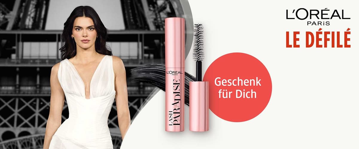 RosĂ©goldene L'OrĂ©al Lash Paradise Mascara mit geöffnetem BĂŒrstenkopf, schwarze Mascara-Striche links, roter Kreis mit Text âGeschenk fĂŒr Dichâ und Schriftzug âL'ORĂAL PARIS LE DĂFILĂâ oben rechts