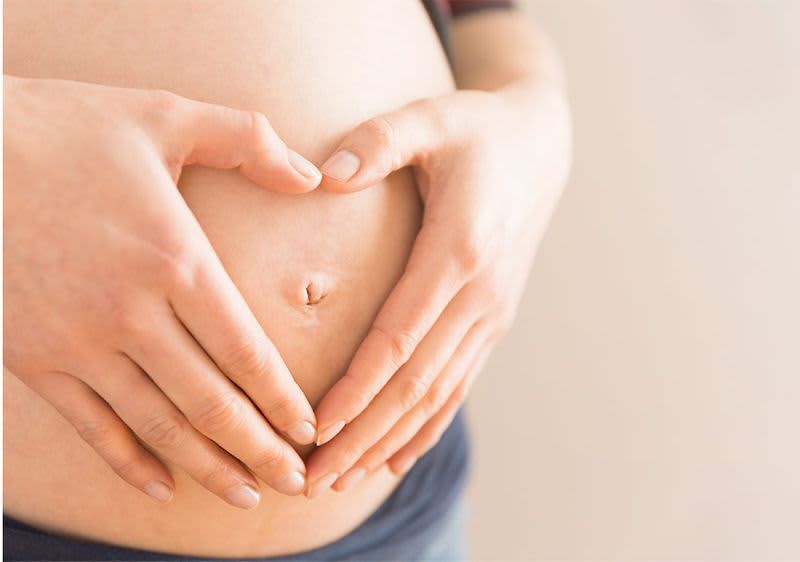 Schwangere legt Hand herzförmig auf ihren Bauch