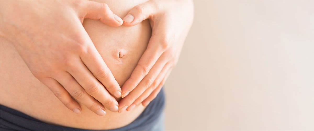 Schwangere legt Hand herzförmig auf ihren Bauch