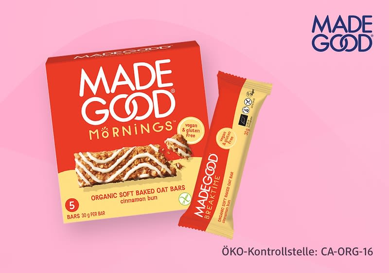 Rote Verpackung der Marke MADE GOOD Mornings mit Bild eines Zimt-Hafer-Riegels; daneben ein einzelner beige-roter Riegel mit der Aufschrift „MADEGOOD“ und Hinweis „organic soft baked oat bars cinnamon bun“ sowie Text „ÖKO-Kontrollstelle: CA-ORG-16“