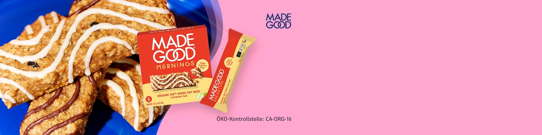 Rote Packung und Riegel der Marke „MADE GOOD“ mit Aufschrift „MORNINGS“ und „Organic soft baked oat bars cinnamon bun“, daneben einzelverpackter Riegel in rot-gelber Folie, rechts oben Logo „MADE GOOD“, unten Schrift „ÖKO-Kontrollstelle: CA-ORG-16“