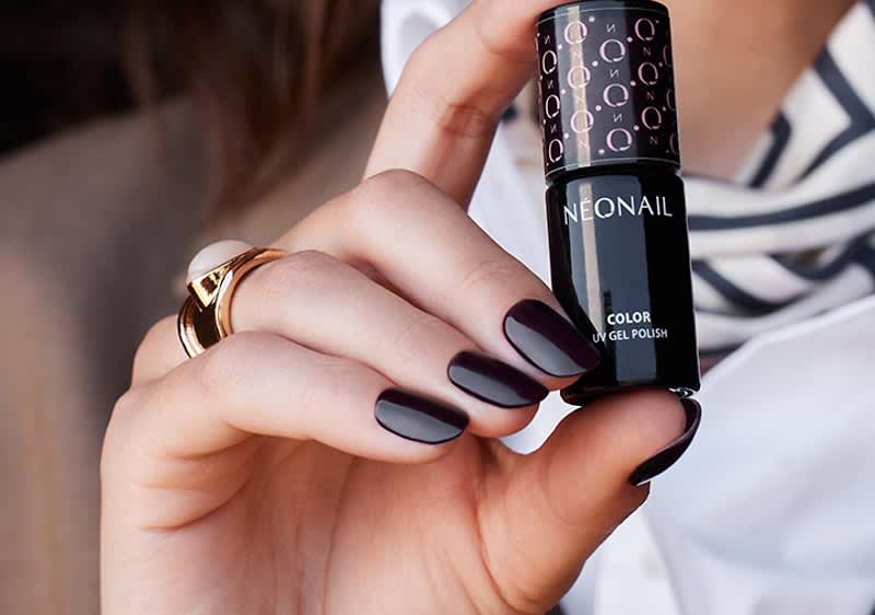 Hand mit dunkellackierten, ovalen Fingernägeln hält eine schwarze Nagellack-Flasche der Marke NEONAIL mit silberner Aufschrift und Muster am Verschluss