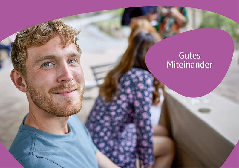 Ein lächelnder Mann sitzt seitlich im Vordergrund, im Hintergrund eine Frau mit floralem Kleid auf einer Parkbank, rechts Text in lila Blase: „Gutes Miteinander“