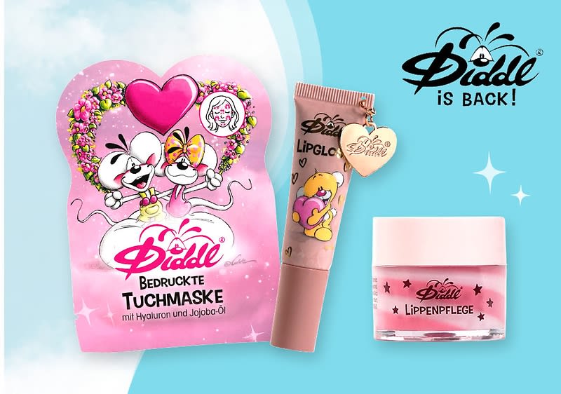 rosa Verpackung einer bedruckten Diddl-Tuchmaske mit Herzmotiv, daneben ein Lipgloss in Tubenform mit Anhänger und Comicmotiv sowie ein kleines Glas mit Lippenpflege, auf hellblauem Hintergrund