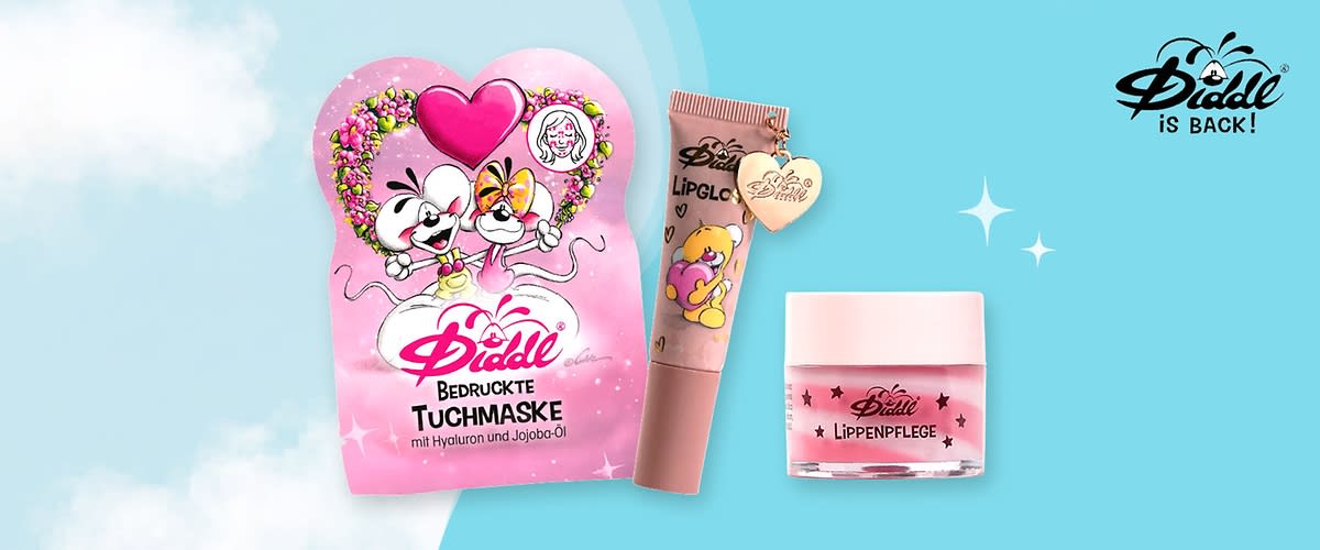 rosa Verpackung einer bedruckten Diddl-Tuchmaske mit Herzmotiv, daneben ein Lipgloss in Tubenform mit Anhänger und Comicmotiv sowie ein kleines Glas mit Lippenpflege, auf hellblauem Hintergrund