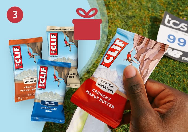 Hand hält einen roten Clif Bar-Riegel mit Aufschrift „Crunchy Peanut Butter“, daneben drei weitere Clif Bar-Packungen in den Sorten „Chocolate Chip“ und „Crunchy Peanut Butter“ vor hellem Hintergrund und Rasen