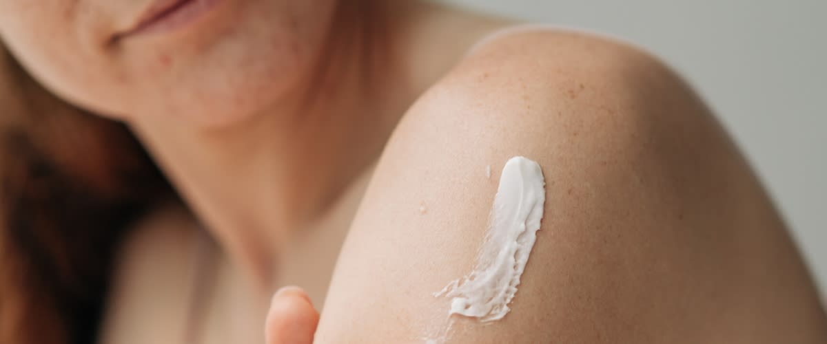 Frau trägt mit Finger eine weiße Creme auf die freiliegende Schulter auf