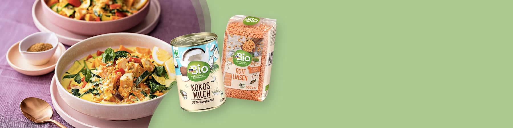 Dose Kokosmilch (dmBio) neben Packung rote Linsen (dmBio) vor zwei Schalen Currygericht mit Gemüse und Zitronenscheiben