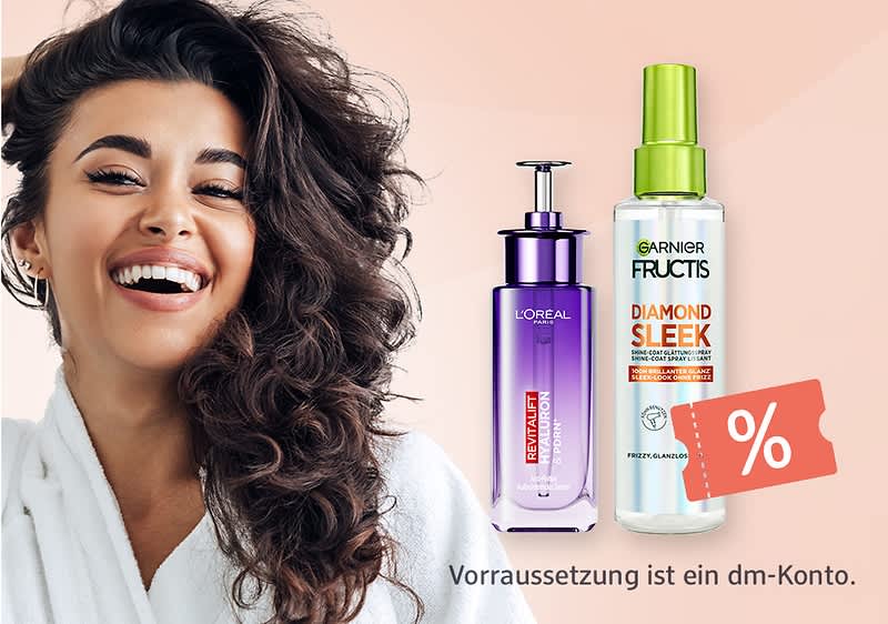 Frau mit langen lockigen Haaren und Morgenmantel lächelt neben zwei Haarpflegeprodukten, links lila L’Oréal-Spenderflasche mit Aufschrift „REVITALIFT LIPIDATION“, rechts Garnier Fructis Spray „DIAMOND SLEEK“, unten Schriftzug „Voraussetzung ist ein dm-Konto.“
