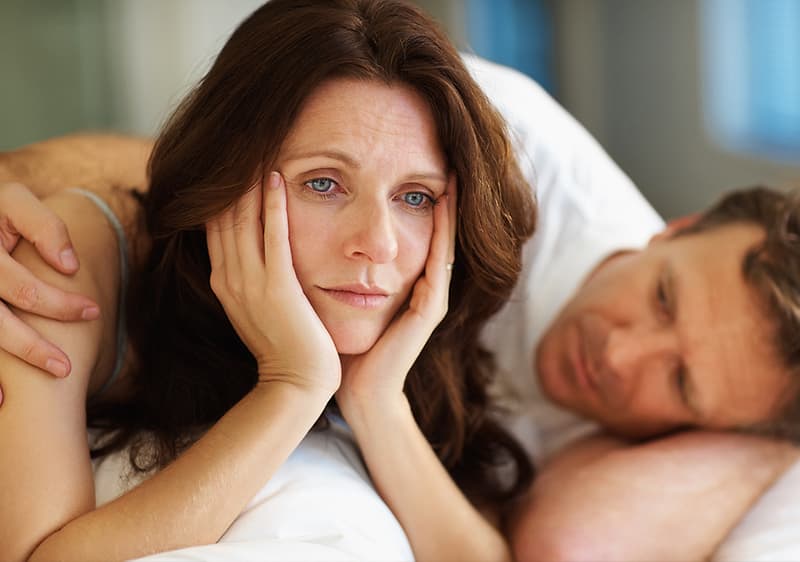 Frau liegt nachdenklich im Bett neben einem Mann