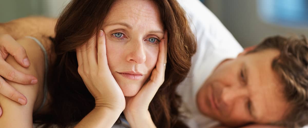 Frau liegt nachdenklich im Bett neben einem Mann