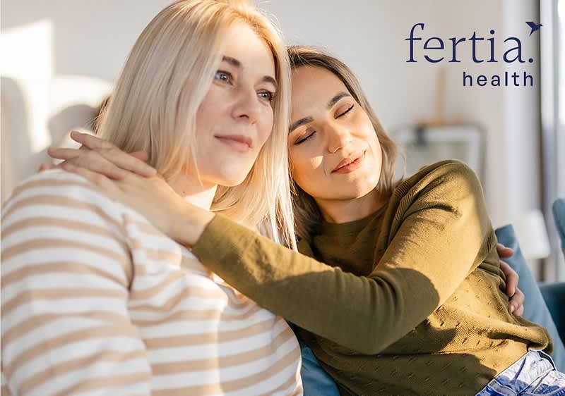 Zwei auf einem Sofa sitzende Frauen, die eine umarmt die andere von der Seite