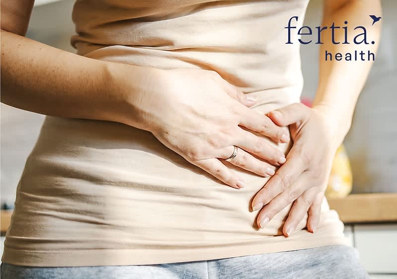 Frau hält beide Hände im Bereich des Unterbauchs, oben rechts Schriftzug „fertia. health“