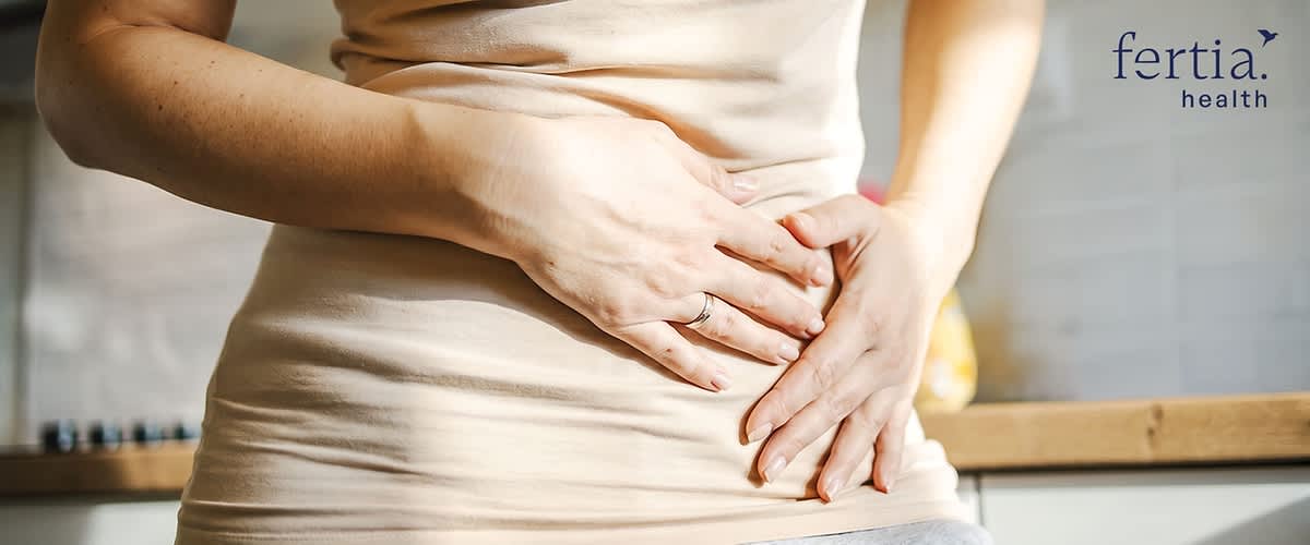 Frau hält beide Hände im Bereich des Unterbauchs, oben rechts Schriftzug „fertia. health“