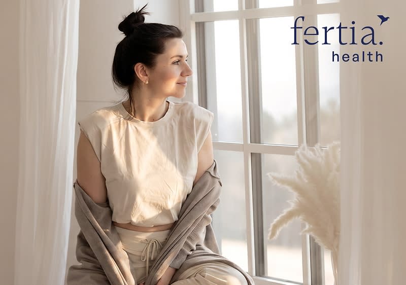 Frau sitzt entspannt auf einer Fensterbank, trägt helle Loungewear und einen offenen Cardigan, Blick nach rechts aus dem Bild